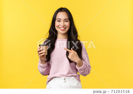 People emotions, lifestyle leisure and beauty concept. Smiling good-looking asian girl pointing at takeaway cup, recommend great cafe with delicious coffee and desserts, yellow background 71201516