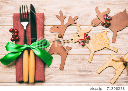 Top view of new year utensils on napkin with holiday decorations and reindeer on wooden background. Close up of christmas dinner concept Top view of new year utensils on napkin with holiday decorations and reindeer on wooden background. Close up of christmas dinner concept 71206228
