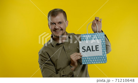Man showing Sale word inscription with shopping bag, smiling, rejoicing discounts on Black Friday 71210648