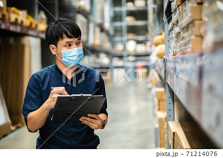 man worker with medical mask holding clipboard and checking inventory in warehouse during coronavirus (covid-19) pandemic 71214076