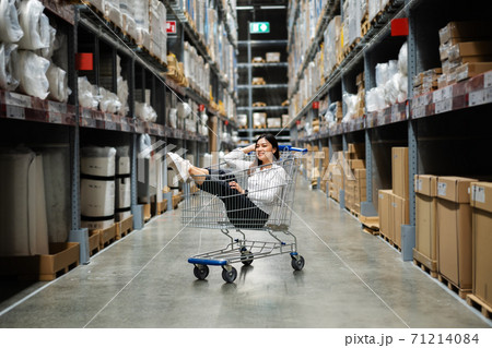 cheerful woman sitting in shopping cart at warehouse store 71214084