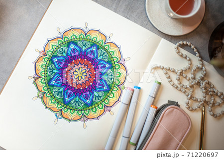 Top view of colored mandala art book with colorful markers, pen, pink pen case and rosary beads. 71220697