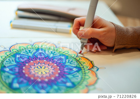 Young woman colouring mandala with markers and white rosary on table with cup of coffee at home 71220826