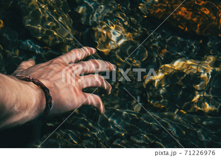 Close-up of a hand touching the surface of the water with light reflections Close-up of a hand touching the surface of the water with light reflections 71226976
