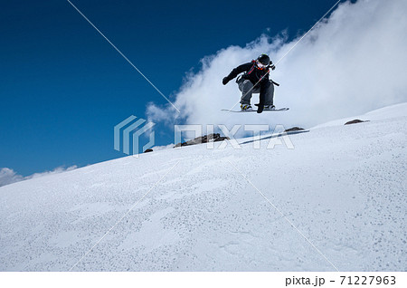 Young woman on a snowboard makes a flight after jumping from a snowy ledge against a dark blue sky high in the mountains in winter 71227963