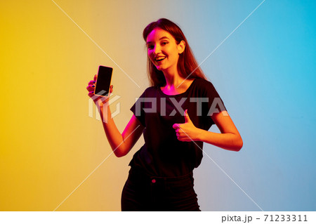 Young caucasian woman's portrait on gradient blue-yellow studio background in neon light Young caucasian woman's portrait on gradient blue-yellow studio background in neon light 71233311