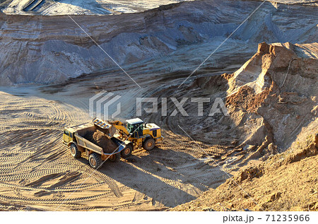 Wheel front-end loader unloading sand into heavy dump truck at the opencast mining quarry 71235966