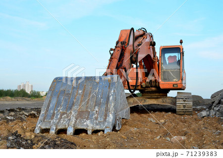 Excavator with a large iron bucket breaks asphalt on a construction site.  71239383