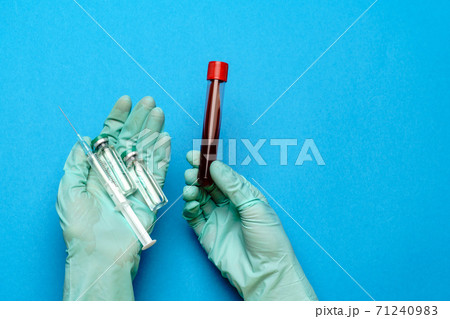 lab technician assistant or doctor wearing rubber or latex gloves holding an ampoule with medicine or vaccine and test tube with blood sample 71240983