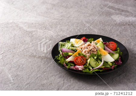 Salad with tuna, egg and vegetables on black plate and gray background Salad with tuna, egg and vegetables on black plate and gray background 71241212