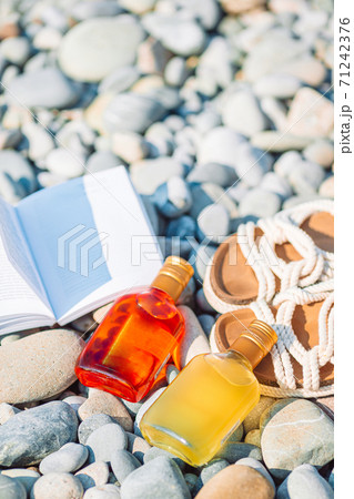 Beach hat on opened book with sunscreen and shoes on pebble beach 71242376