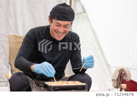 キャンプ場でたこ焼きを焼くアジア人男性 71254679