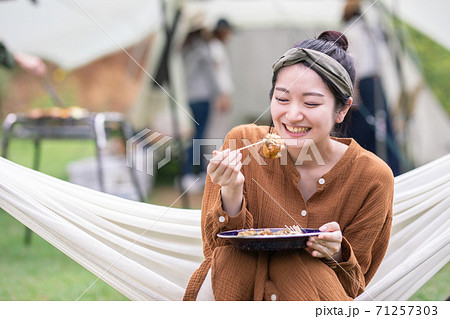 キャンプ場でハンモックに乗りながらたこ焼きを食べるアジア人女性 71257303