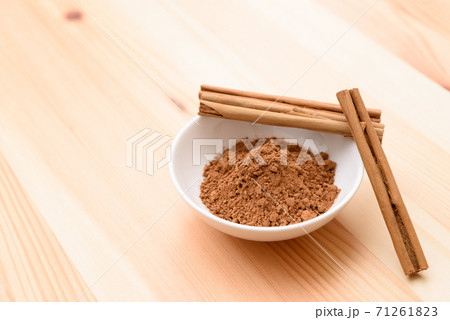 木目テーブルにある皿の上のシナモンスティックとシナモンパウダーの写真素材