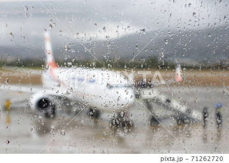 Blurred image of the aircraft at the airport through the glass covered with raindrops Blurred image of the aircraft at the airport through the glass covered with raindrops 71262720