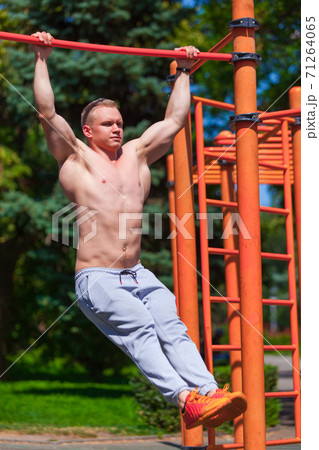 Strong muscular man with a bare torso pulls himself up on a crossbar. Working out outdoors in summer park 71264065