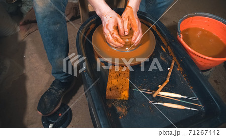 Potter works with clay on wheel in workshop. 71267442