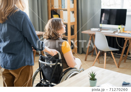 Young businesswoman pushing wheelchair with her disable female colleague 71270260