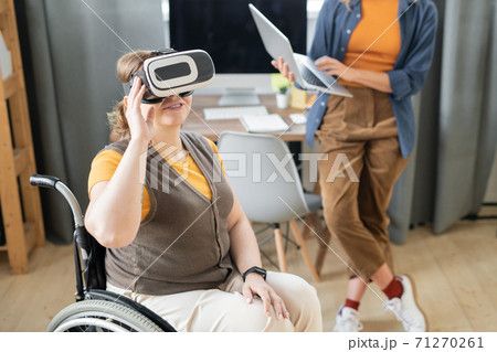 Disable businesswoman in vr headset sitting in wheelchair against busy colleague 71270261