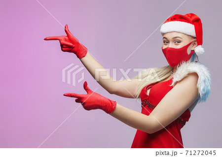 young girl in a Santa hat, red mask and gloves shows the direction with her index fingers. Christmas and the concept of covid-19 prevention young girl in a Santa hat, red mask and gloves shows the direction with her index fingers. Christmas and the concept of covid-19 prevention 71272045