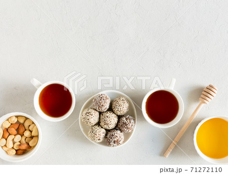 Homemade raw candy energy balls with almond, cashews, peanut butter and hazelnuts on the plate with tea cups flat lay on gray background with copy space. Organic snack. Vegetarian food. 71272110