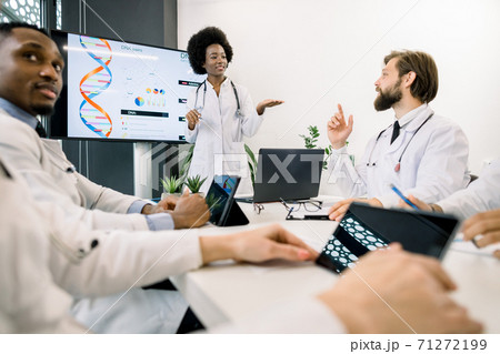 Concept of research and testing, medicine, genetics. Pretty young focused African female scientist discussing about the chromosome deseases or DNA testing with her Caucasian male colleague on meeting 71272199