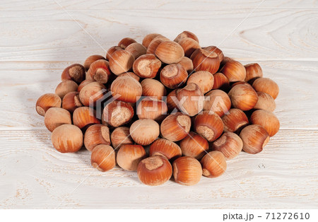 Pile of unpeeled hazelnuts over white wood table. 71272610