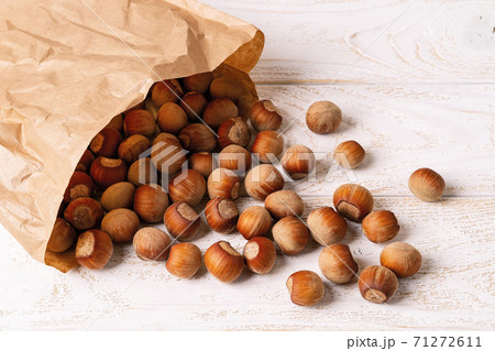 Unpeeled hazelnuts spilled out of a paper bag onto the white wood table. Unpeeled hazelnuts spilled out of a paper bag onto the white wood table. 71272611