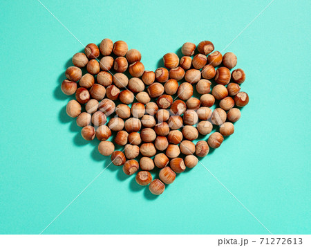 Heart shape made of unpeeled hazelnuts casts shadows on a turquoise paper background. Heart shape made of unpeeled hazelnuts casts shadows on a turquoise paper background. 71272613