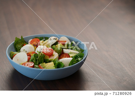 Salad with avocado, cherry tomatoes, romaine and mozzarella in blue bowl on walnut table with copy space 71280926