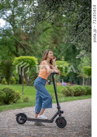 Long-haired cute girl resting on her scooter and speaking on the phone Long-haired cute girl resting on her scooter and speaking on the phone 71285858