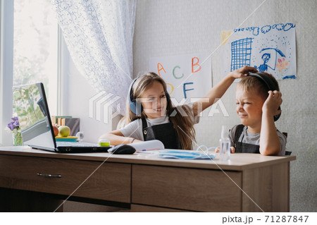 Distance learning, home education, remote lessons concept. Two schoolchildren, brother and sister in headphones sit near open laptop and watch a video lesson, listen to the teacher Distance learning, home education, remote lessons concept. Two schoolchildren, brother and sister in headphones sit near open laptop and watch a video lesson, listen to the teacher 71287847