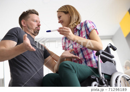 Woman in wheelchair happily smiles at man and holds pregnancy test man looks surprised. 71296189