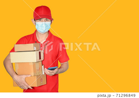 Delivery man employee cap and shirt red uniform face mask holder parcel Box Mail box isolated on yellow background Service New normal after pandemic coronavirus concept 71296849