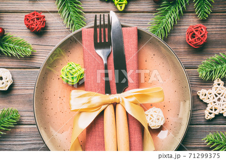 Holiday composition of plate and flatware decorated with Santa hat on wooden background. Top view of Christmas decorations. Festive time concept Holiday composition of plate and flatware decorated with Santa hat on wooden background. Top view of Christmas decorations. Festive time concept 71299375