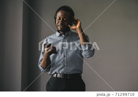 Young african man listening to music with wireless earphones and dancing at home 71299710