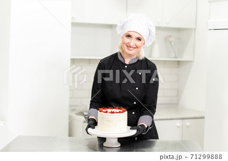 Portrait of friendly smiling female professional confectioner topping a cupcake with cream using a pastry bag Portrait of friendly smiling female professional confectioner topping a cupcake with cream using a pastry bag 71299888