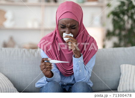 Sick black muslim woman with runny nose checking body temperature at home 71300478