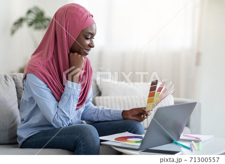 Smiling Black Muslim Lady Holding Color Swatch And Using Laptop At Home Smiling Black Muslim Lady Holding Color Swatch And Using Laptop At Home 71300557