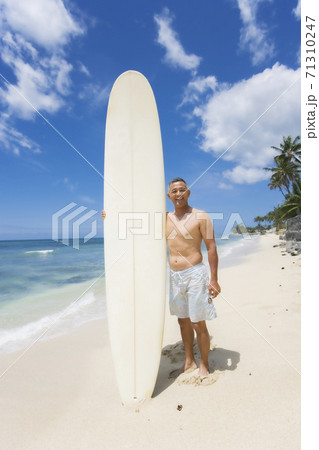サーフボードを持って海辺に立つシニア男性の写真素材