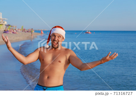 New year's eve on the beach by the sea. happy man in a Christmas hat sunbathing in the sun. blue sky as a copy of space 71316727