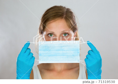 Woman stretching ear loops of blue surgical mask as she is attaching it 71319530