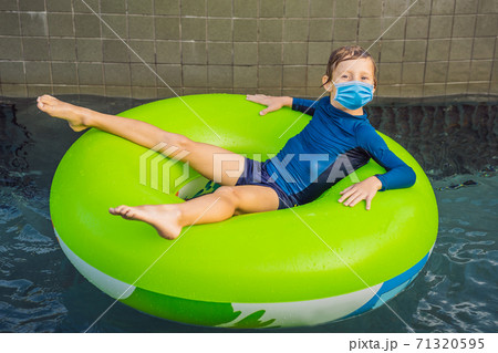 Little boy wearing a medical mask during COVID-19 coronavirus swimming with rubber ring at the leisure center Little boy wearing a medical mask during COVID-19 coronavirus swimming with rubber ring at the leisure center 71320595