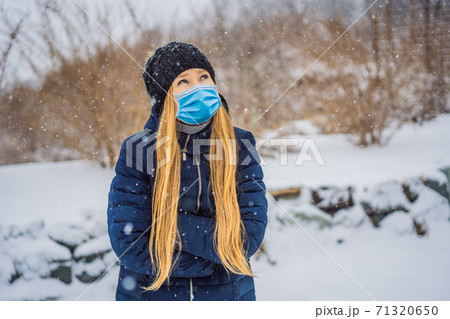 The woman wearing a medical mask during COVID-19 coronavirus was very froze in winter under snowfall. Winter problems 71320650