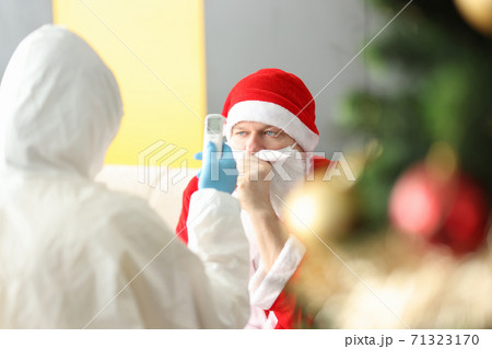 Doctor in protective suit and rubber gloves measuring temperature of sick Santa Claus with an infrared non-contact thermomete Doctor in protective suit and rubber gloves measuring temperature of sick Santa Claus with an infrared non-contact thermomete 71323170
