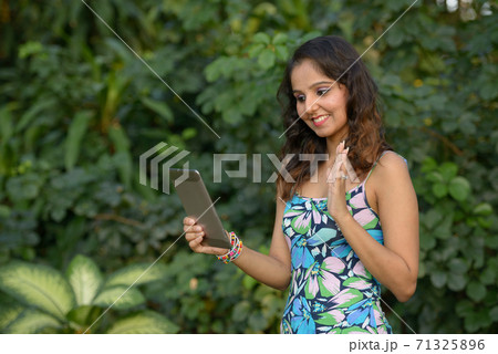 Happy young beautiful Indian woman video calling with digital tablet at the park 71325896