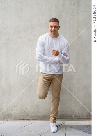 Full body shot of happy handsome man leaning against concrete wall 71326657
