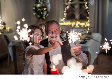 Senior grandfather with small granddaughter indoors at Christmas, having fun with sparklers. 71326762