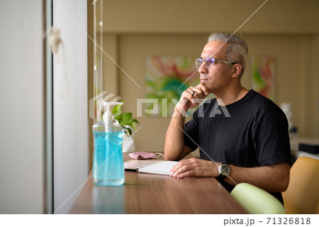 Handsome Persian man with gray hair thinking while writing at the library Handsome Persian man with gray hair thinking while writing at the library 71326818