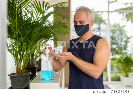 Mature Persian man with mask using hand sanitizer while social distancing at the gym 71327143